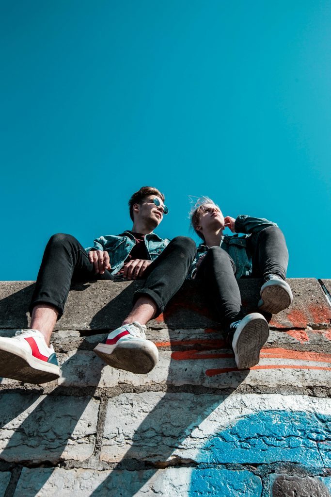 pexels-photo-1019771-1019771 Two young people sitting on a stone wall under a vibrant blue sky, enjoying a sunny day together.