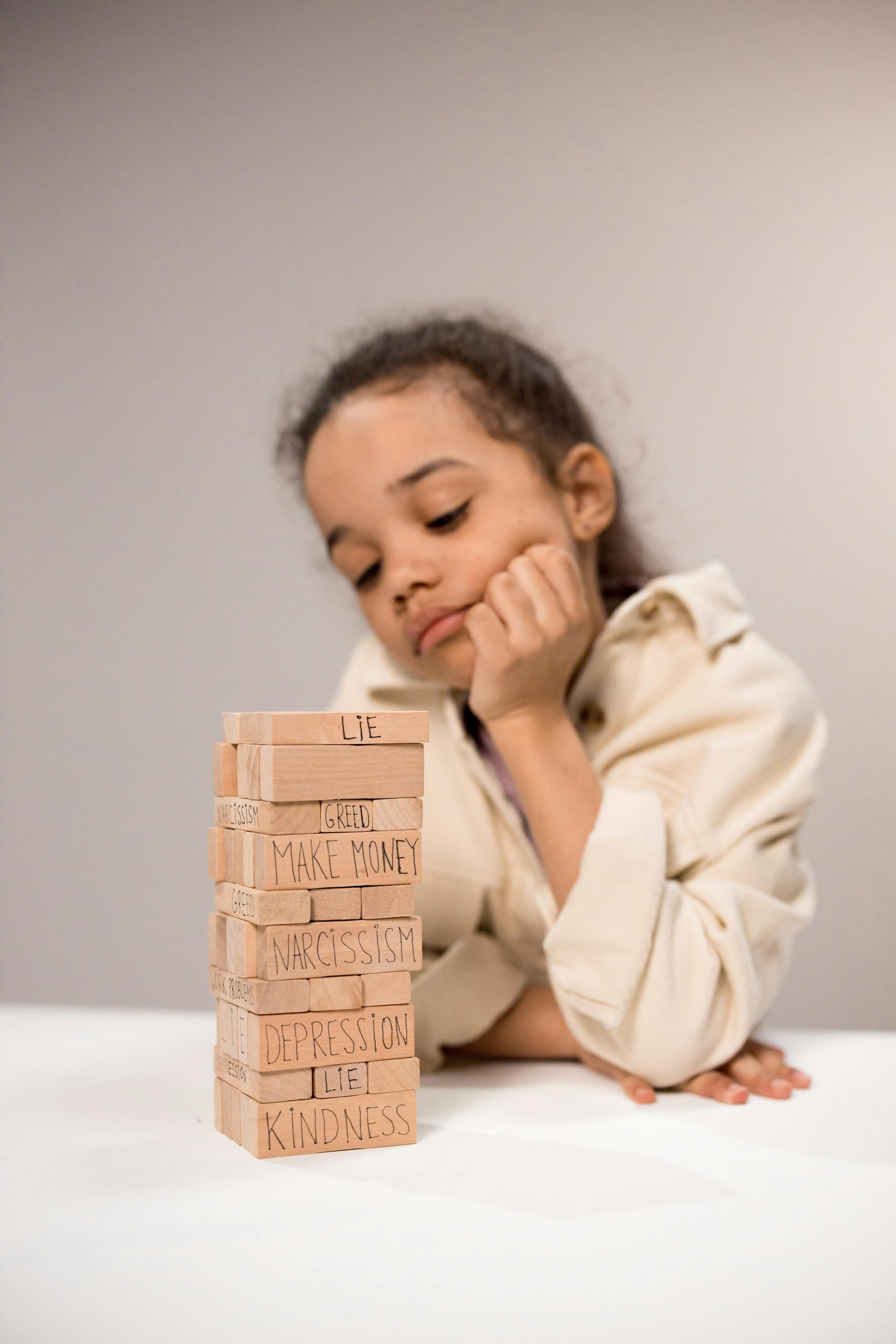 A young girl contemplates a stack of wooden blocks with words like 'lie' and 'kindness.'