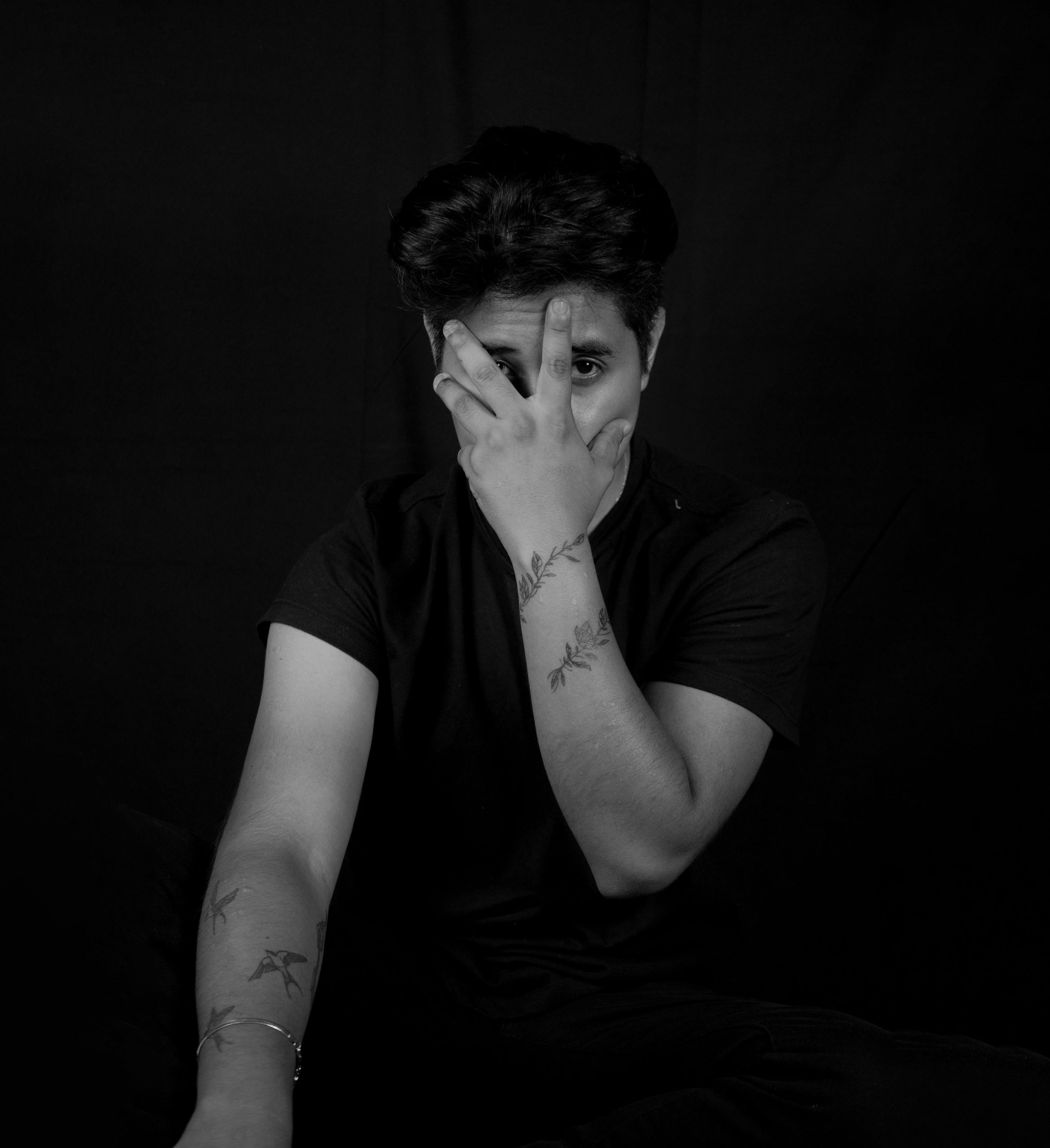 Artistic black and white portrait of a tattooed man posing with hand on face.